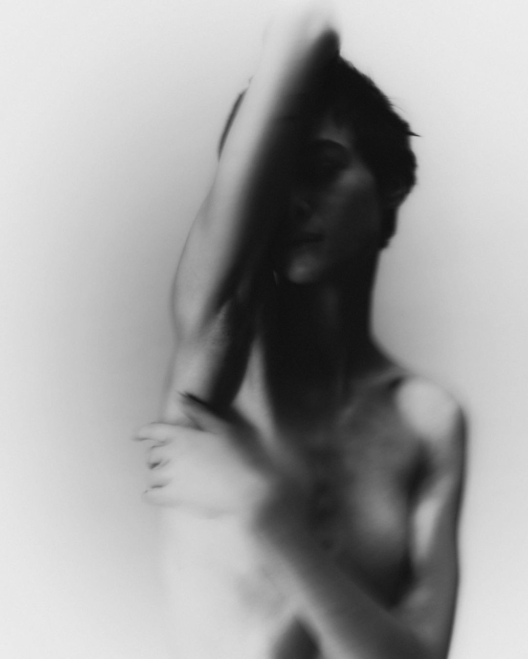 Monochrome portrait of a person with arms raised, blurred motion effect against a white background