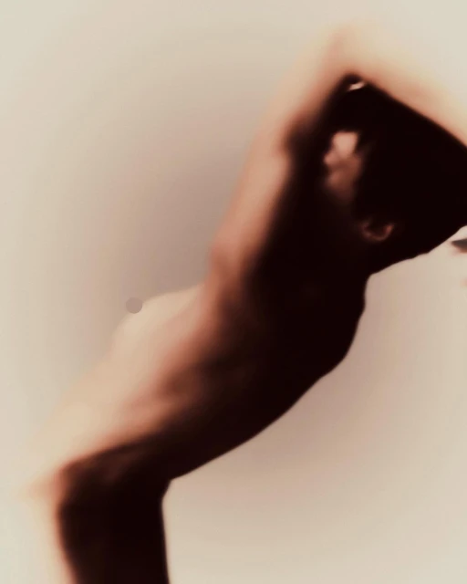 Abstract soft focus artistic shot of a topless adult male with arms overhead posing in a photo studio with neutral background and soft lighting.