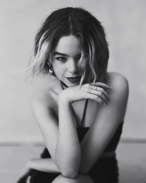 Black and white portrait of a young woman with wavy bob haircut, wearing a crop top and jewelry, posing with hands near her face.