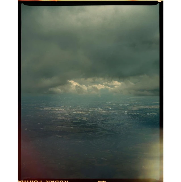 Aerial view showcases expansive cloudscape above a city, with soft light filtering through the clouds, cityscape visible below.