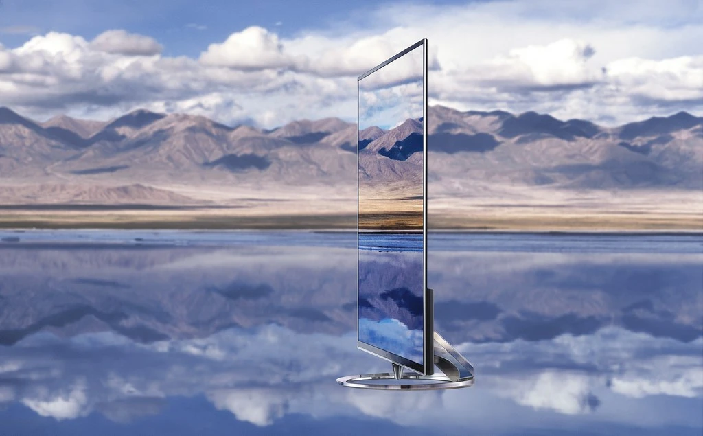 Sleek flat-screen television displays landscape scene with mountains and lake against blurred background of mountains and cloudy sky.