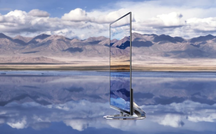 Sleek flat-screen television displays landscape scene with mountains and lake against blurred background of mountains and cloudy sky.