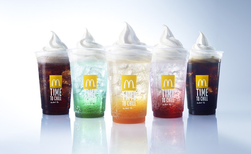 A row of McDonald's drinks with soft serve, including cola, green soda, orange soda, and red soda, displayed against a white background.