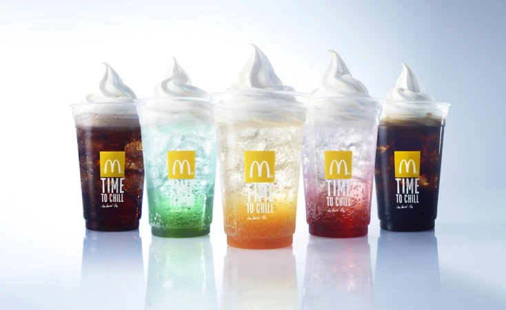 A row of McDonald's drinks with soft serve, including cola, green soda, orange soda, and red soda, displayed against a white background.