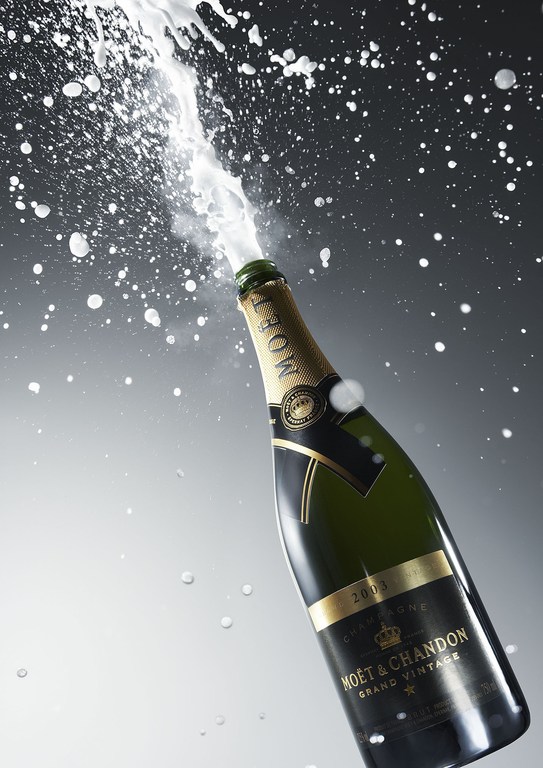 Champagne bottle explodes with foam and splashes against a graduated gray background, showcasing celebration, luxury, and effervescence.