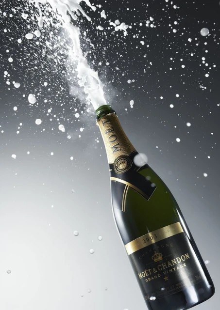Champagne bottle explodes with foam and splashes against a graduated gray background, showcasing celebration, luxury, and effervescence.
