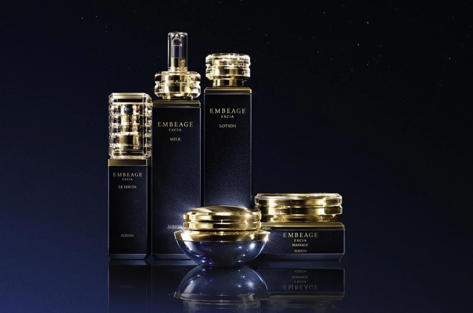 Luxury skincare product line featuring Embeage Excia lotion, milk, serum, and massage cream in dark bottles with gold accents on a reflective surface.