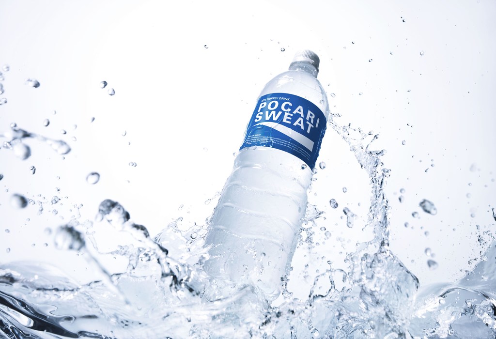 Pocari Sweat bottle with water splash in a bright studio shot. Clear plastic bottle, blue label, water droplets and splash effect.