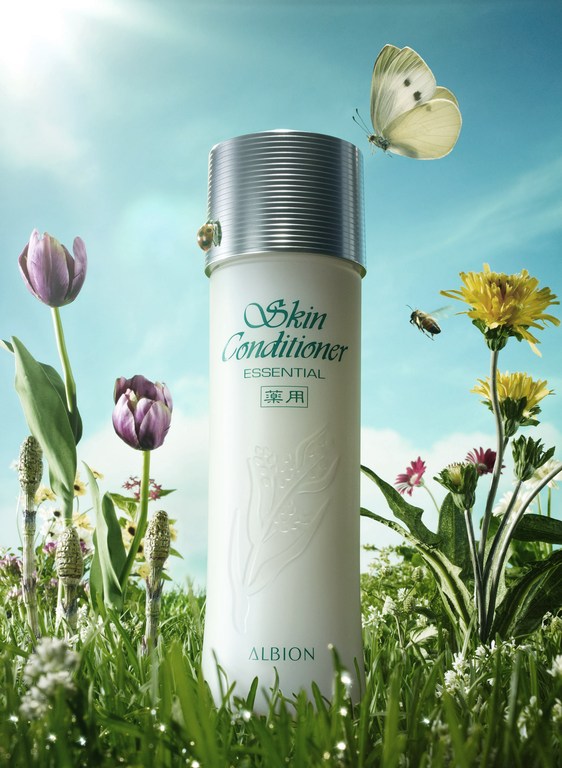 White Albion skin conditioner bottle stands in a field of green grass with a butterfly and a bee against a blue sky backdrop.