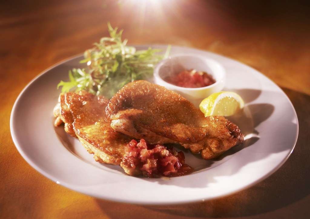 Overhead shot of plated meal featuring crispy-skinned chicken, fresh salad, red relish, and lemon slice, presented on a white ceramic plate.