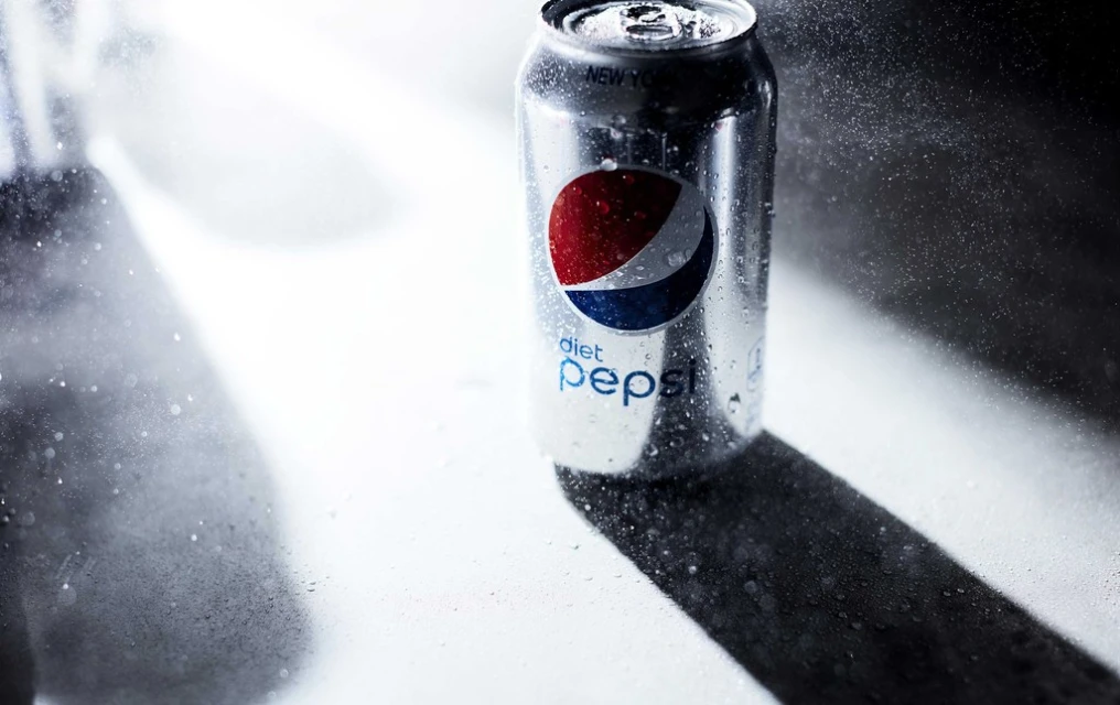 Studio shot of a silver Diet Pepsi can with condensation, casting a dramatic shadow on a white surface with a dark backdrop.
