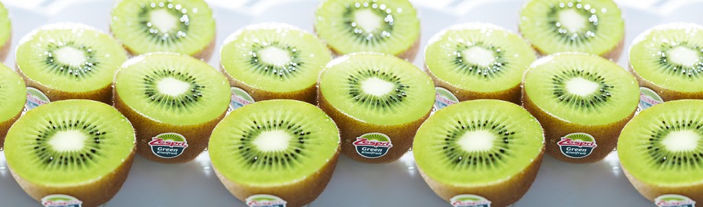 Close-up of multiple halved Zespri green kiwifruit slices arranged in rows, with a white background, showcasing their vibrant green color.
