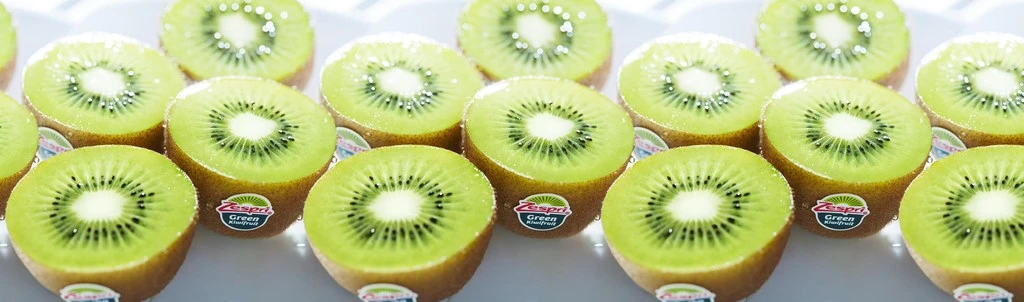 Close-up of multiple halved Zespri green kiwifruit slices arranged in rows, with a white background, showcasing their vibrant green color.