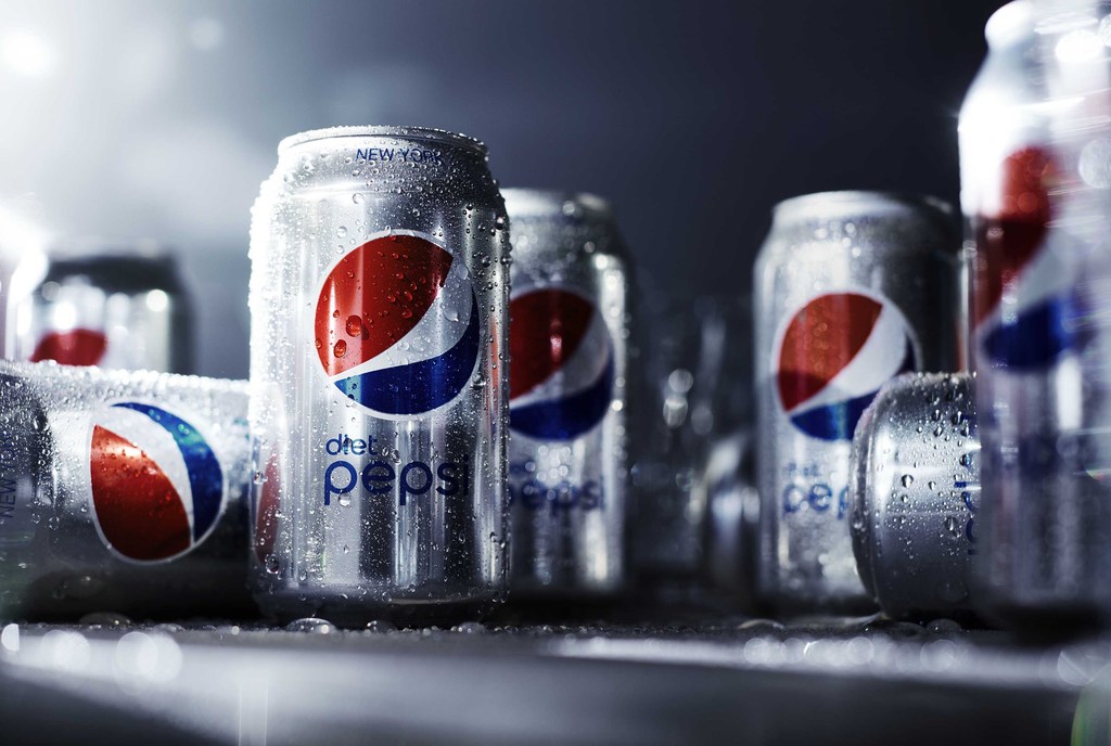 Several silver cans of Diet Pepsi arranged in a group, some with condensation, against a blurred, dark background.