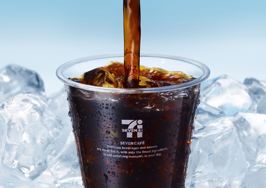 Iced coffee being poured into a clear plastic cup, set against a background of ice and a light blue gradient.