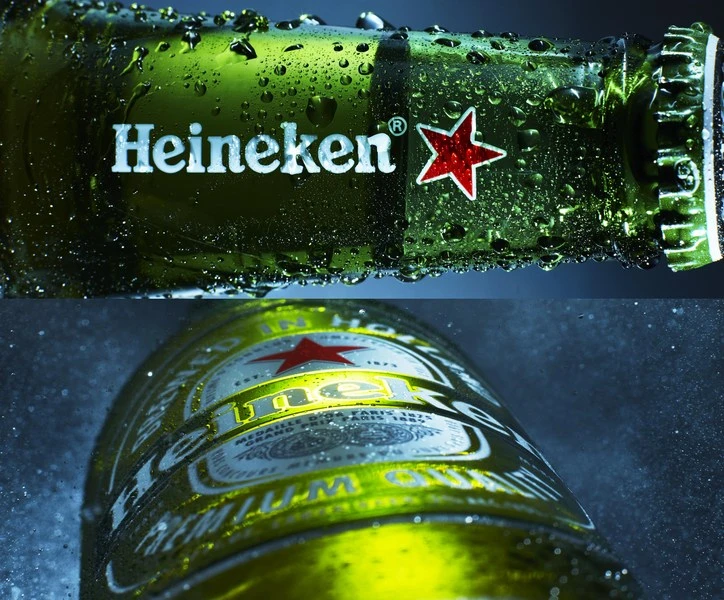 Macro studio shot of a wet green glass Heineken beer bottle with a red star logo and droplets against a dark blue background.