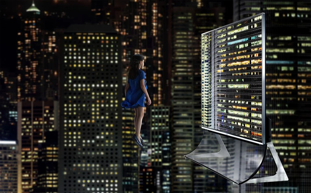 Girl stands before a digital display showing city lights at night, creating a surreal cityscape. Dark background with illuminated buildings.