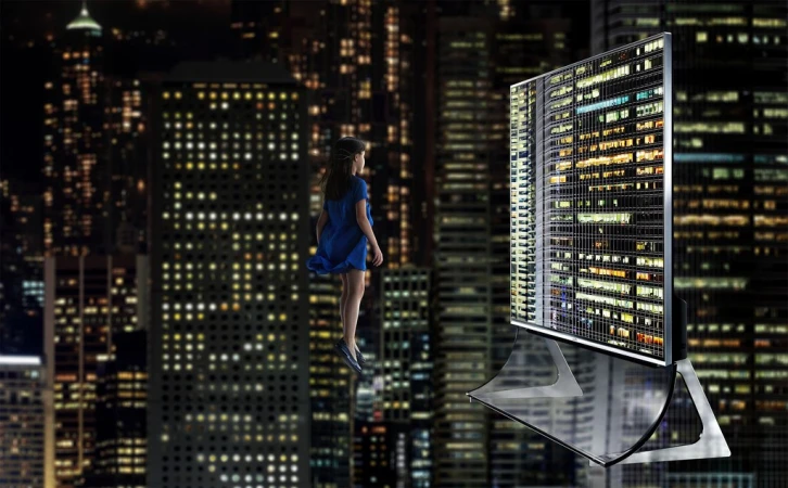 Girl stands before a digital display showing city lights at night, creating a surreal cityscape. Dark background with illuminated buildings.