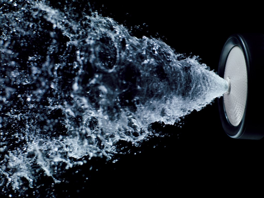 Water spraying from a black speaker on a black background, creating a dynamic and visually striking high-speed water photography effect.
