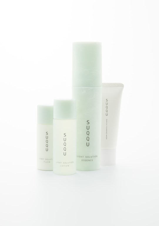 Four bottles of SUQQU skincare products are arranged on a white surface, including cleanser, lotion, and essence, in a beauty still life.