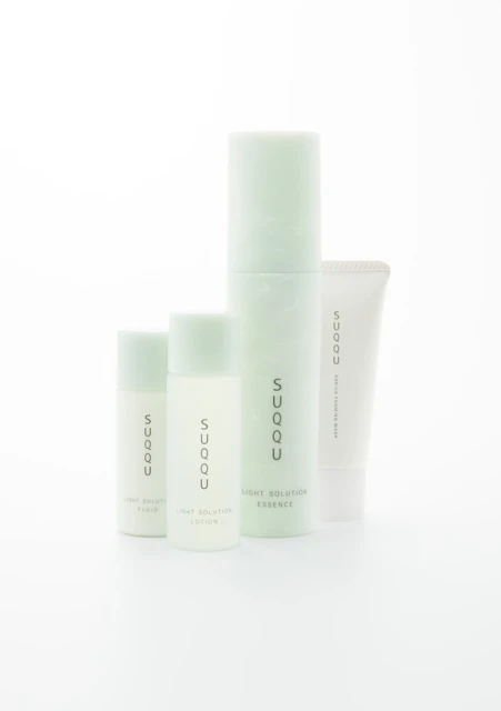 Four bottles of SUQQU skincare products are arranged on a white surface, including cleanser, lotion, and essence, in a beauty still life.