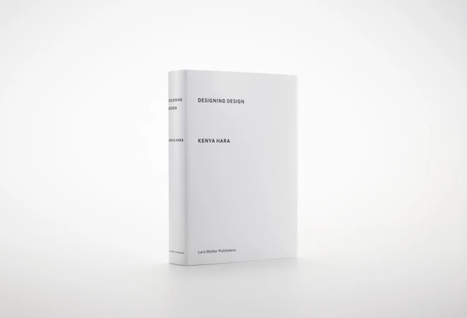 Book titled 'Designing Design' by Kenya Hara on a white surface, featuring a minimalist design and clean typography, standing in a white setting.