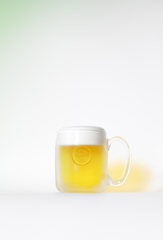 Studio shot of a frosty beer mug with light beer and condensation on a white surface against a soft green and white gradient background.