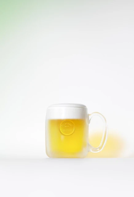 Studio shot of a frosty beer mug with light beer and condensation on a white surface against a soft green and white gradient background.