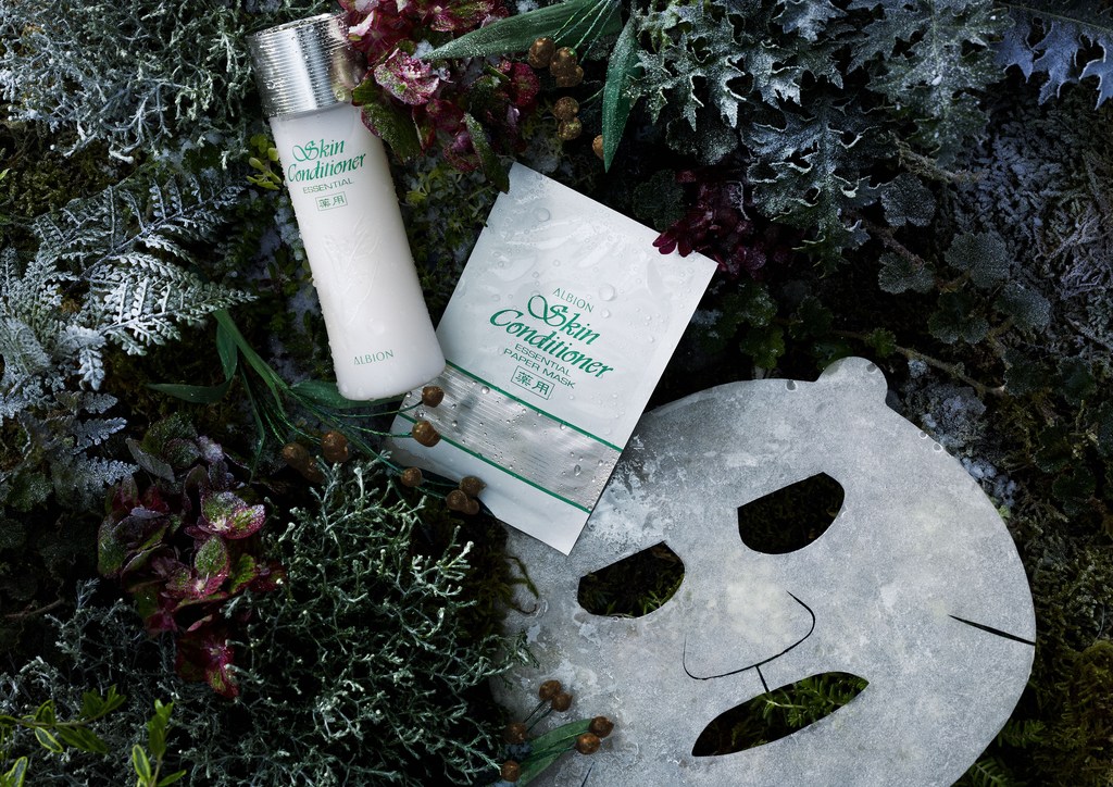 Albion skin conditioner bottle and paper mask on bed of green foliage, berries, and dried leaves; product shot for beauty industry.