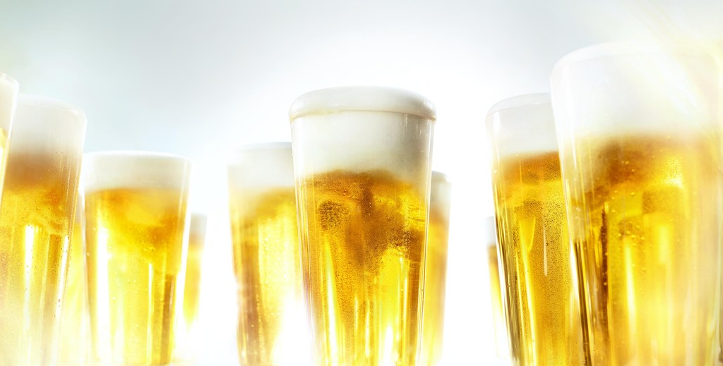 Group of tall beer glasses filled with foamy golden beer, creating a refreshing and celebratory visual. Bright lighting emphasizes the beverage.