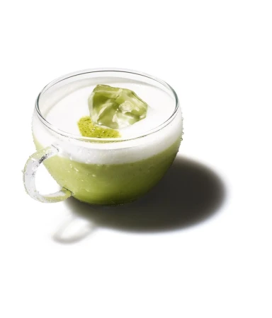 Close-up studio shot of a clear glass cup with matcha latte topped with ice. The drink is on a solid white background.