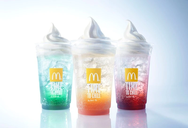 Three McDonald's frozen drinks in clear plastic cups, each featuring a different colorful soda flavor and vanilla soft serve.