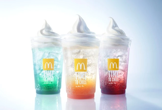 Three McDonald's frozen drinks in clear plastic cups, each featuring a different colorful soda flavor and vanilla soft serve.