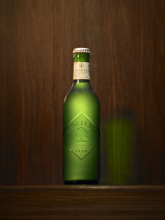A green glass bottle of Portland Beer is illuminated against a dark wooden background, highlighting the label and condensation.