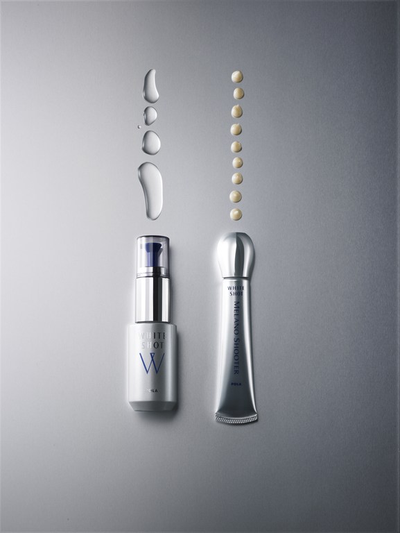 Two silver and white skincare product tubes, one with a blue pump, are showcased with water droplets and product dots on a grey background.