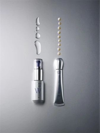 Two silver and white skincare product tubes, one with a blue pump, are showcased with water droplets and product dots on a grey background.