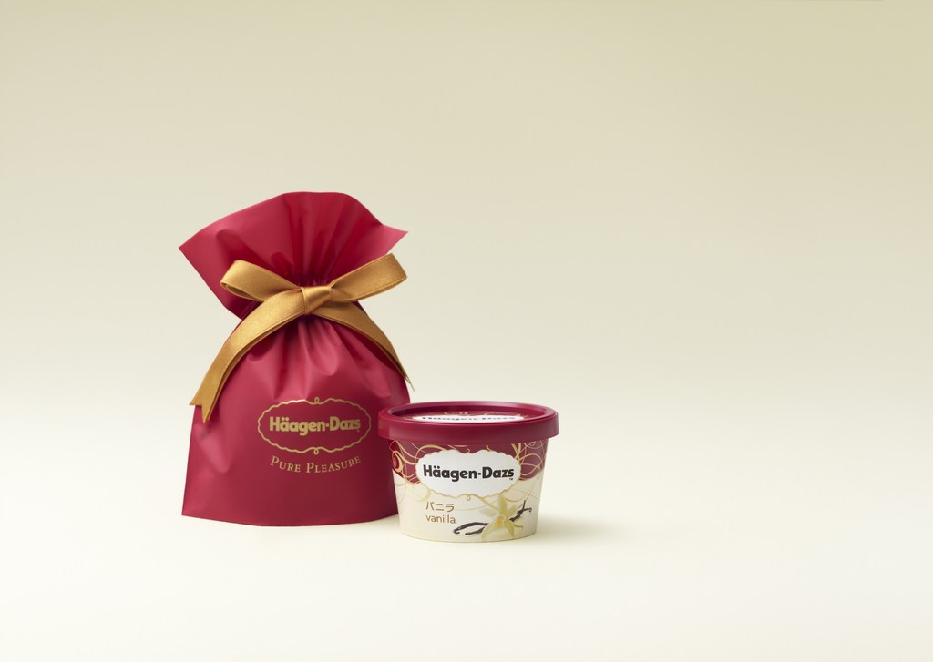 Häagen-Dazs vanilla ice cream in its container sits next to a red Häagen-Dazs gift bag with a gold ribbon on a cream background.