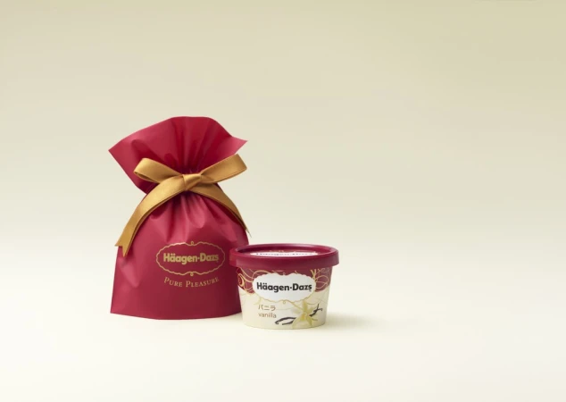 Häagen-Dazs vanilla ice cream in its container sits next to a red Häagen-Dazs gift bag with a gold ribbon on a cream background.
