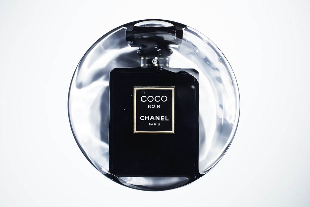 Close-up studio shot of a black 'Coco Noir' Chanel perfume bottle on a clear, glossy surface, highlighting the elegant design and branding.