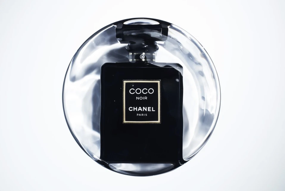 Close-up studio shot of a black 'Coco Noir' Chanel perfume bottle on a clear, glossy surface, highlighting the elegant design and branding.