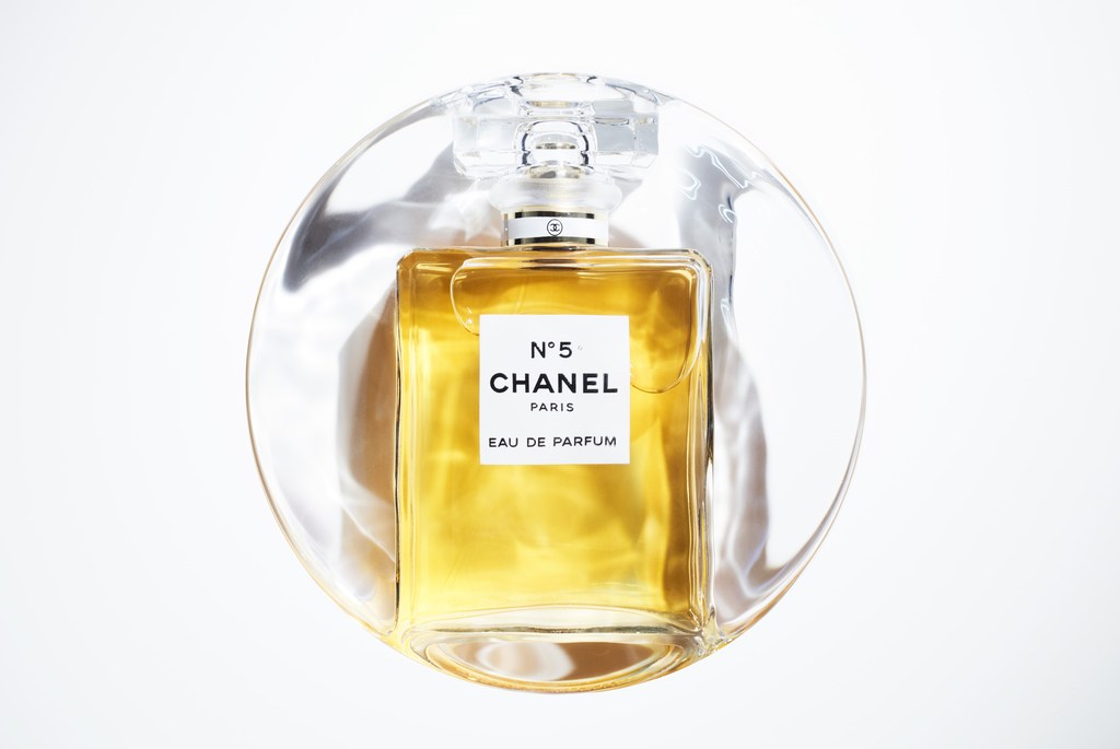 Chanel N°5 Eau de Parfum in a clear glass bottle with a geometric stopper, centered on a white backdrop inside a decorative transparent disc.