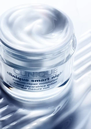 Close-up of Clinique Smart Night moisturizer in a clear jar with white cream, studio lighting, and a cool color palette.