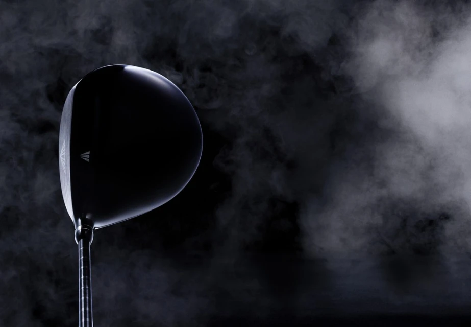 Elevated studio shot showcases a sleek black golf club head against a dark background with smoky gradients, highlighting its modern design.