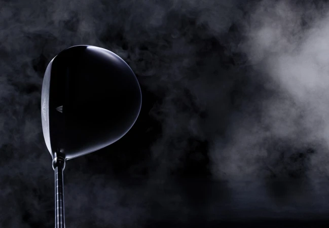 Elevated studio shot showcases a sleek black golf club head against a dark background with smoky gradients, highlighting its modern design.