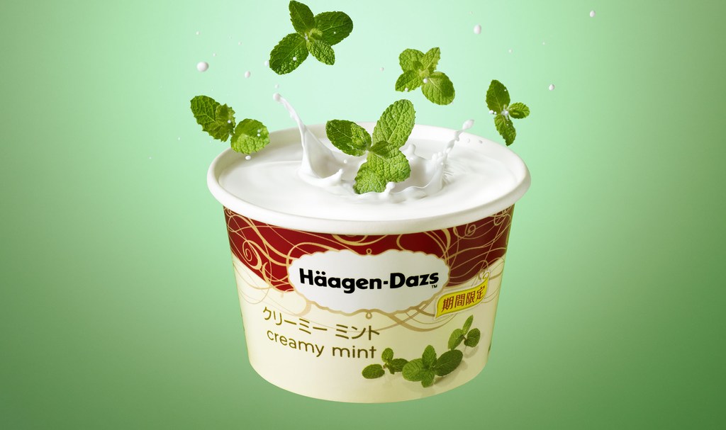 Häagen-Dazs ice cream with mint leaves splashing into it against a green background, capturing a refreshing and tempting dessert scene.