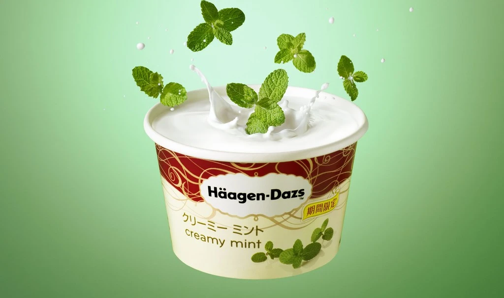 Häagen-Dazs ice cream with mint leaves splashing into it against a green background, capturing a refreshing and tempting dessert scene.