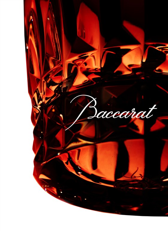 Close-up of Baccarat crystal glass with an angular design, vibrant red and black hues, and the 'Baccarat' logo in elegant white script.