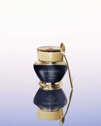 Luxury skincare jar in dark blue with gold cap and matching spoon resting beside it on a reflective gradient surface
