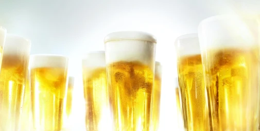 Close-up low-angle view of multiple tall glasses filled with golden beer and thick white foam against a bright white background.