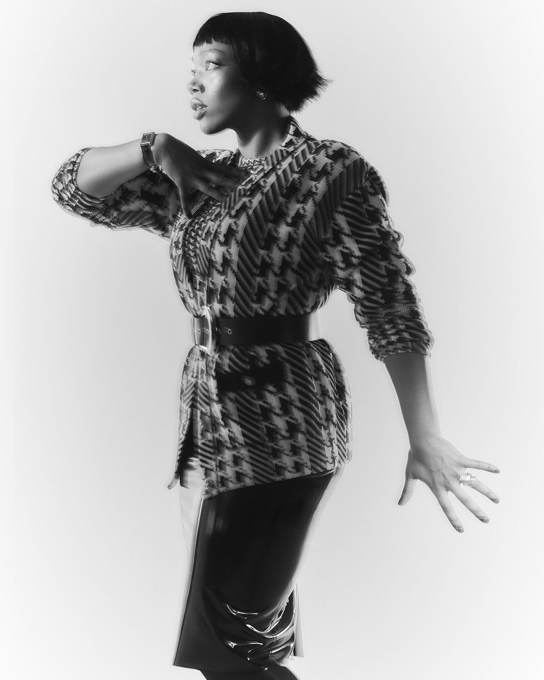 Monochrome portrait of an African-American woman in patterned jacket and black patent skirt, striking a pose against a light background.
